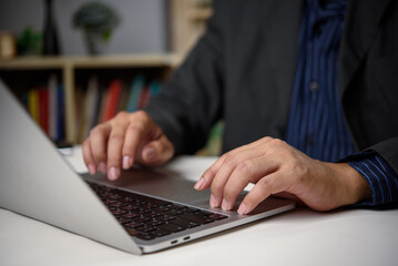 Obraz premium Businessman using laptop in office with bookshelf background. Concept of knowledge work, productivity, and digital online working business in professional environment with modern tech tools.