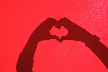 Fototapeta premium Man and woman hands making a heart shape on a red background