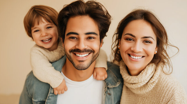 Young Hispanic couple laughing and smiling, with young toddler son, studio shot against beige background