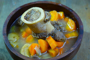 A rich bone marrow soup with chunks of carrots and meat, served in a rustic wooden bowl.