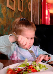 Child girl eating greek salad in cafe. Healthy appetizers lettuce wraps with vegetables, bell...