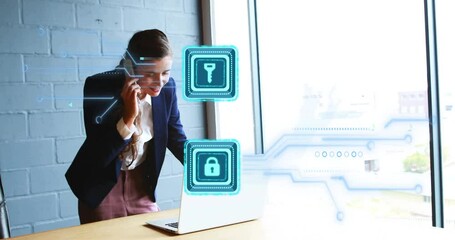 Businesswoman making smartphone call and checking laptop while glowing security icons over window - Powered by Adobe