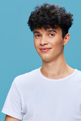 young man with curly hair wearing white t-shirt posing against blue background with subtle smile, casual style, studio portrait, natural lighting