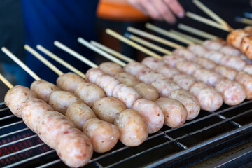 northeastern sausage on stick or skewered and arranged grilled burn on charcoal stove or isan sausage and barbecue meatball with merchant hand for thai street food in local thailand or esan sausages