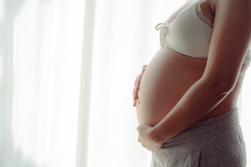 Young happy pregnant woman posing in studio with white curtains in background