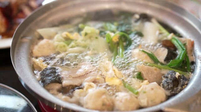 closeup sukiyaki or hot pot to boiling water steam or suki soup bubbles from heat with meatball vegetable and seaweed wrapped meatballs for dinner or lunch at japanese food restaurant in thailand