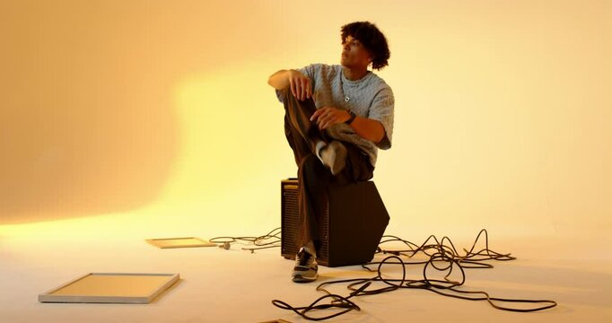 Man resting chin on speaker box then tousling hair and gesturing in amber-lit studio for shoot