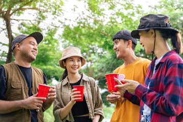 Happy asian diverse group friends enjoy drinking a beer together. They feeling relaxed and refreshing while camping in the nature. Recreation and journey outdoor activity lifestyle.