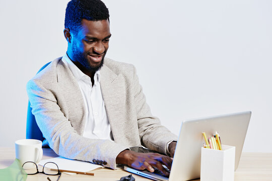 Professional young man working on laptop at desk, smiling and focused, in a modern office environment, casual business attire, workspace with stationery and coffee, concept of remote work and
