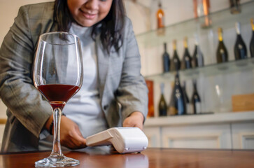 Hispanic woman charging wine with contactless payment in a wine shop