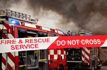 Firefighter emergency services fire engines – red fire truck from fire department with firefighting equipment on appliance from fire station at scene of incident. Smoke in air from a burning building. © Lawrey