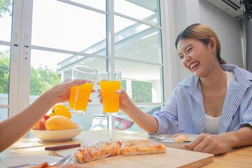 Two elegant young women sit in a house, smiling and clinking glasses of juice and breakfast of positive friendship, bonding and unity.