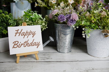 Happy Birthday text on paper card with flowers decoration on wooden background