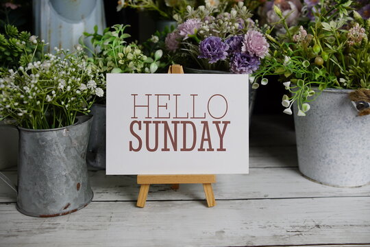 Hello Sunday text on paper card with flowers decoration on wooden background