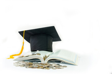 A graduation cap rests on an open book, with a pile of coins in front of it.