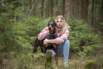 Portrait of young beautiful blonde girl with Doberman outdoors.