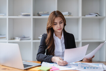 Focused businesswoman analyzes documents at her desk in a bright office space