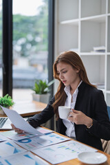 Professional woman reviews financial reports with coffee at her office desk.