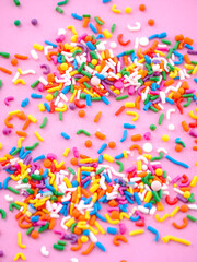 Colorful sprinkles scattered on pink background. (4)