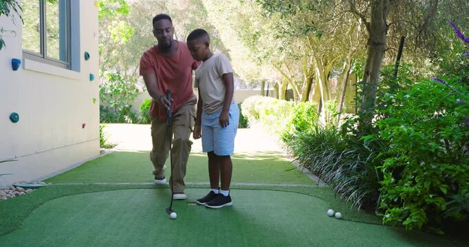 African American father and son putting on mat in yard showing putter grip celebrating putt