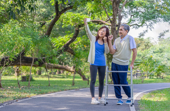 A daughter take care senior to rehab with walker walking in the park,cheerful woman taking selfie together with her father,bonding family,relationship