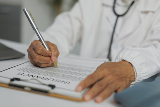 Close up of doctor's hands filling insurance claim form, providing healthcare coverage and financial protection for patients undergoing medical treatment