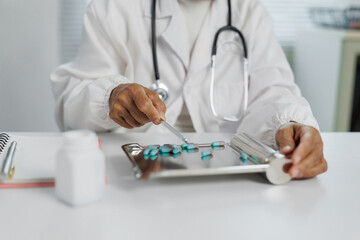 Doctor wearing a stethoscope is carefully arranging blue and white pills on a metal counting tray,...