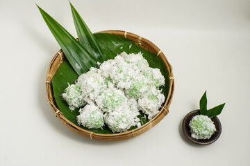 Indonesian klepon rice balls with grated coconut, served in bamboo tray and ceramic plate on white...
