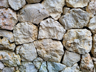 Close-up of a rustic stone wall made from irregularly shaped natural rocks with earthy tones and...