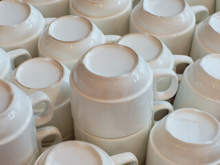 Clean white ceramic coffee mugs stacked upside down in bulk, arranged neatly for service in a café, hotel, or buffet environment, ready for use.