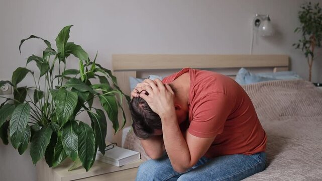 Sad Man Sitting On Bed In Bedroom Touching Head Because Of Headache Or Emotional Experience. Grief, Crying And Depression.