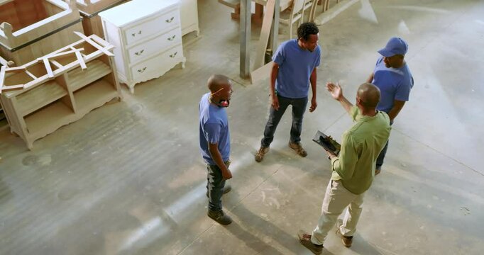 African American man leading workers as unfolding clipboard plan and assigning tasks in workshop
