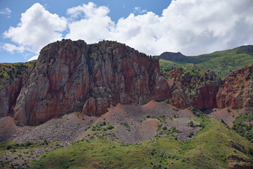 Scenic view of a rugged rocky cliff under a bright blue sky in a dry mountainous region. Natural textures, arid landscape, and distant hills create a stunning outdoor wilderness scene.