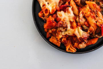 cheesy pasta bake with mediterranean vegetables and beans on black plate