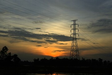 High voltage power lines silhouetted against a dramatic sunset sky, transmitting electricity and...
