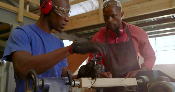 African American instructor mounting blank on lathe, guiding apprentice shaping wood in workshop