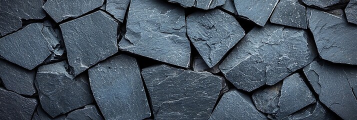 Fototapeta premium Dark slate stones arranged in an overlapping pattern, creating a textured, natural stone wall surface.
