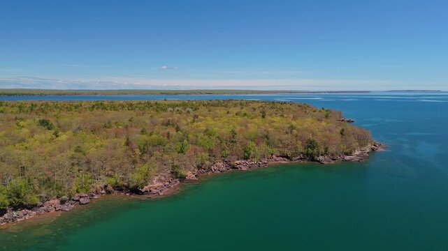 A breathtaking view of Madeline Island Lake Superior shoreline, with crystal-clear turquoise water, rocks, and vibrant spring trees, perfect for a scenic getaway
