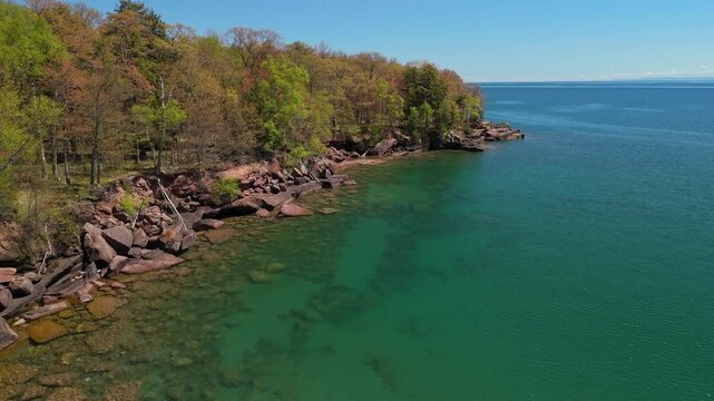 A breathtaking view of Madeline Island Lake Superior shoreline, with crystal-clear turquoise water, rocks, and vibrant spring trees, perfect for a scenic getaway