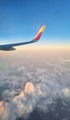 Airplane Wing High Above White Fluffy Clouds at Sunset. View From Plane Window During Flight.