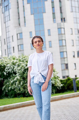 Fototapeta premium A woman in a white shirt and blue jeans walks along the city streets. She has a beautiful athletic figure. The concept of confidence and style. The concept of fashion.