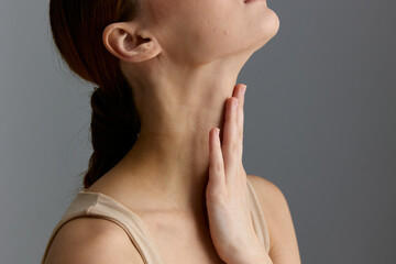 Close-up of a woman touching her neck with a contemplative expression, soft natural lighting, beige...