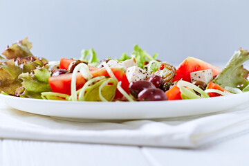 Simple salad with cherry tomatoes, feta cheese, kalamata olives, red pepper and fresh herbs. Bright wooden background. Close up.	