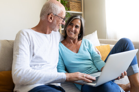 Mature married couple in love using laptop relaxing on the sofa looking at each other smiling.