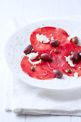 Slices of beef carpaccio with olives and capers. Close up.	