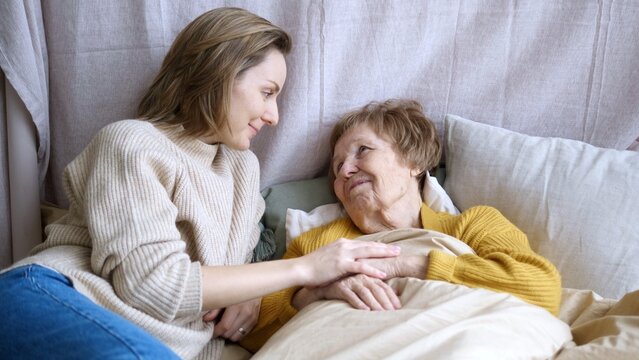 Young woman comforting her elderly mother, offering compassionate home care and support, holding her hand with warmth and empathy, strengthening their bond during this intimate moment