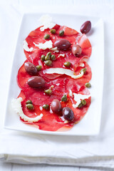 Slices of beef carpaccio with olives and capers. Close up.	