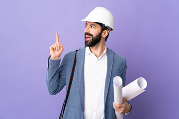 Young architect man with helmet and holding blueprints over isolated purple background thinking an idea pointing the finger up