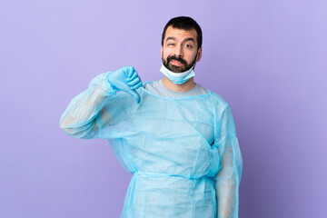 Surgeon man with beard with blue uniform over isolated purple background showing thumb down with...