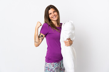 Young slovak woman isolated on white background in pajamas and holding a pillow and celebrating a...